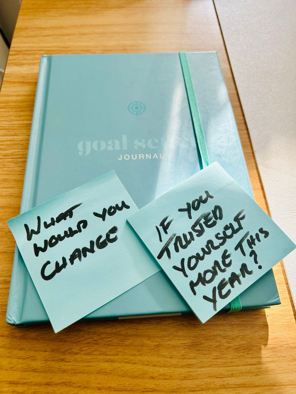 A teal goal-setting journal with sticky notes about reflection and self-trust.