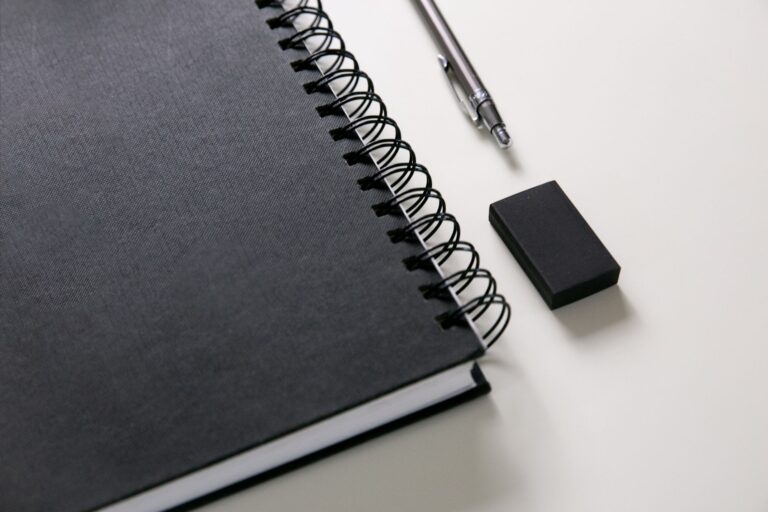 A dark notebook, pen, and eraser arranged as a quiet reflection still life.
